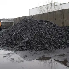 Kupa węgla na placu z koparką i betonowym murem.