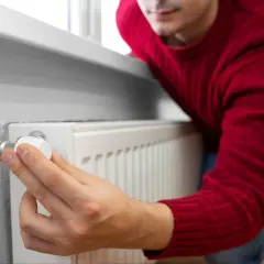 Mężczyzna w czerwonym swetrze reguluje termostat grzejnika, oszczędzając na rachunkach dzięki bonowi ciepłowniczy.