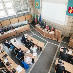 Obrady rady miasta, podczas których odbywa się udzielenie absolutorium. Ludzie siedzą przy stołach, niektórzy pracują na laptopach.
