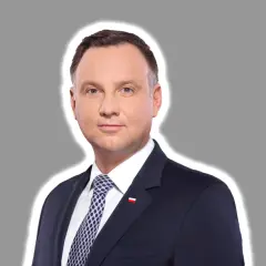 Prezydent Andrzej Duda w garniturze, z biało-czerwoną flagą na klapie. Jego twarz wyraża powagę, jakby rozważał kwestię ułaskawienia.