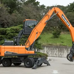 Pomarańczowy koparko-ładowarka z chwytakiem, model DX 270 WMH. To sprzęt firmy Develon, znanej z produkcji maszyn budowlanych.