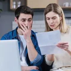 Para zmartwiona analizuje dokumenty przy laptopie.