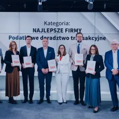 Grupa osób w garniturach i sukienkach odbiera dyplomy na tle ekranu z napisem "Kategoria: Najlepsze Firmy".