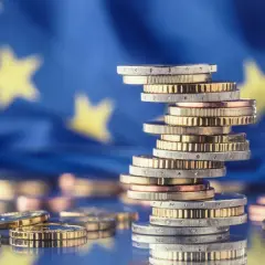 Stos monet euro na tle flagi UE symbolizuje pomoc de minimis dla przedsiębiorców.