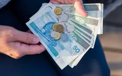 Dłonie trzymają polskie banknoty i monety. Symbolizują one wsparcie finansowe, jak renta rodzinna dla wdowy po ukończeniu 50 lat.