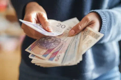 Ręce liczą polskie banknoty. Zastanawiasz się, ile wzrośnie emerytura z OFE po 65 roku życia?