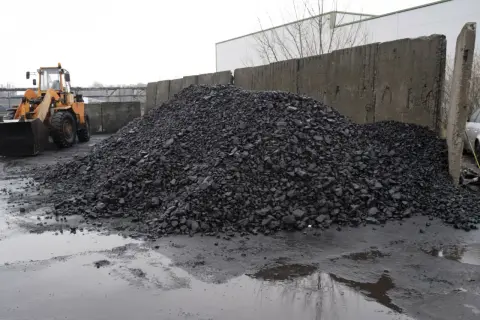 Kupa węgla na placu z koparką i betonowym murem.