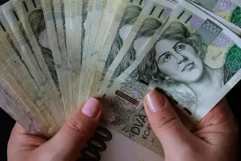 Dłonie trzymające stos banknotów 2000 koron czeskich. Czy to znak, które banki są zagrożone upadłością w Polsce?