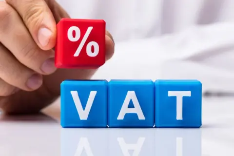 Dłoń układa kostkę z symbolem procentu na kostkach z literami VAT. Rozważasz usługę gastronomiczną a VAT?