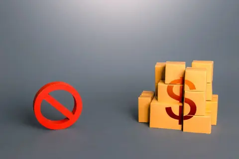 Czerwony znak zakazu obok stosu pudełek z symbolem dolara.