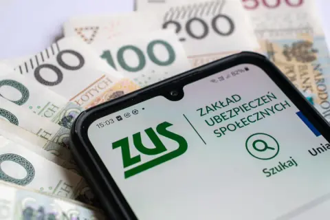 Pracujący emeryt sprawdza na telefonie aplikację ZUS, analizując przeliczenie emerytury na tle polskich banknotów.
