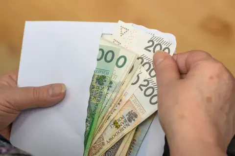 Dłonie wyciągają z koperty polskie banknoty. To może być pomoc z ZUS, np. renta rodzinna po mężu.