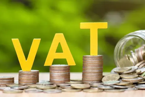 Żółte litery VAT na stosach monet, obok słoik pełen pieniędzy. Grupa vat to ważny element finansów.
