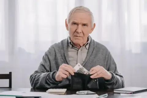Starszy mężczyzna z portfelem w ręku, liczy pieniądze. Czy to na wcześniejszą emeryturę?