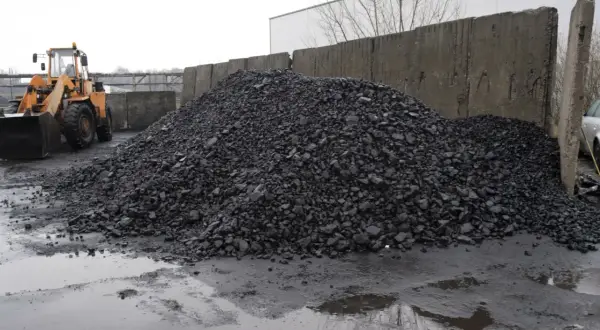 Kupa węgla na placu z koparką i betonowym murem.