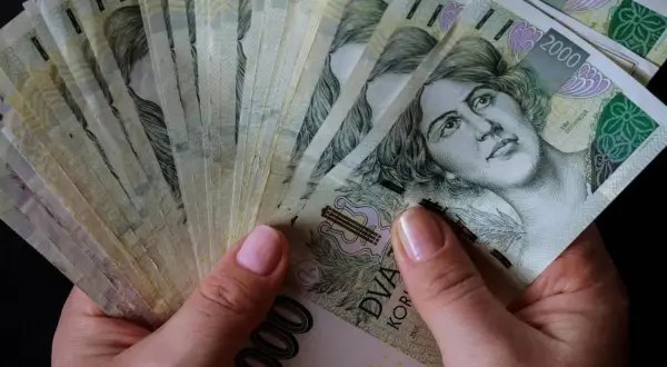 Dłonie trzymające stos banknotów 2000 koron czeskich. Czy to znak, które banki są zagrożone upadłością w Polsce?