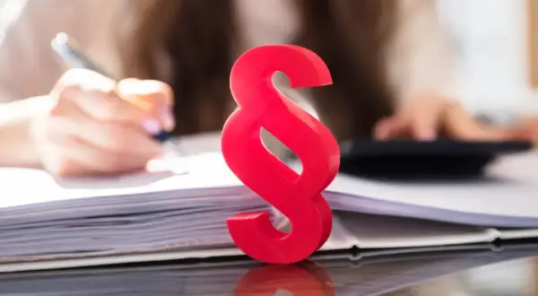 Czerwony paragraf symbolizuje prawne aspekty, gdy firma ogłasza upadłość, co z pracownikami? Tło pokazuje ręce pracujące przy dokumentach i kalkulatorze.