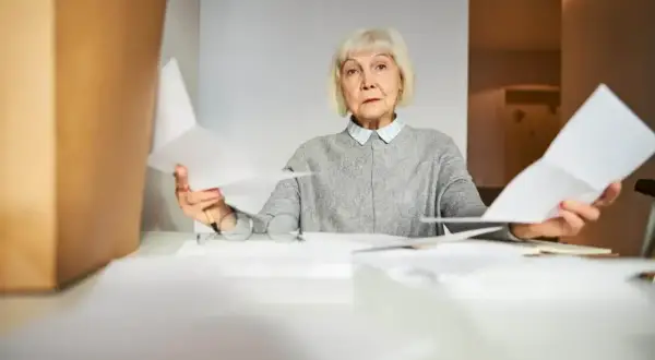 Zmartwiona starsza pani z dokumentami w rękach zastanawia się, czy renta wlicza się do emerytury.