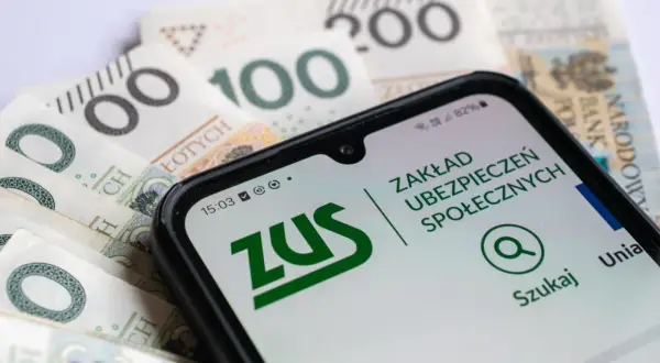 Pracujący emeryt sprawdza na telefonie aplikację ZUS, analizując przeliczenie emerytury na tle polskich banknotów.
