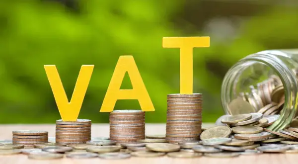 Żółte litery VAT na stosach monet, obok słoik pełen pieniędzy. Grupa vat to ważny element finansów.