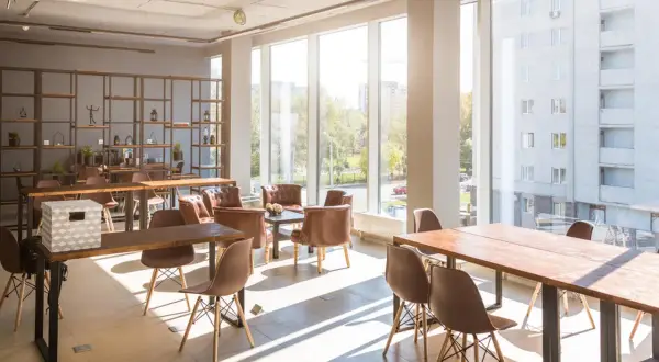 Jasne, nowoczesne wnętrze z dużymi oknami, stołami i krzesłami. Idealne miejsce na coworking, które może być świetnym lokalem inwestycyjnym.