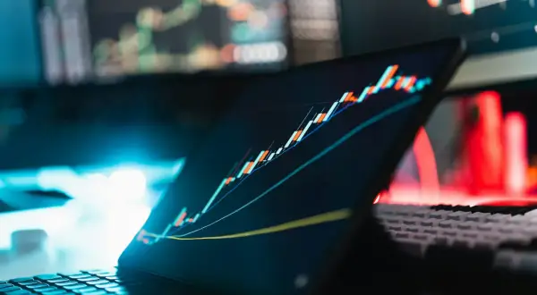 Analiza wykresów giełdowych na ekranie tabletu i monitorów. W tle czerwone i niebieskie światła. To może być inspiracja, jak napisać projekt o dofinansowanie.