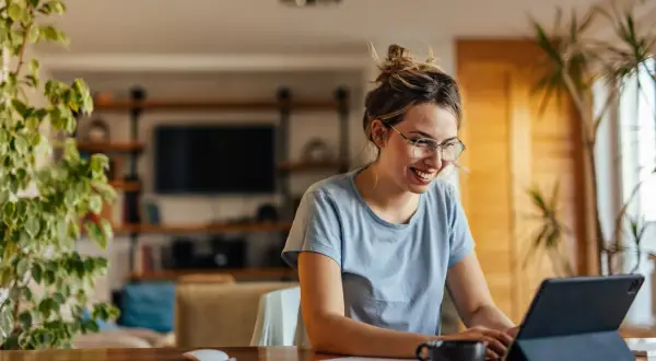 Uśmiechnięta kobieta w okularach pracuje na tablecie, być może przedłuża umowę.