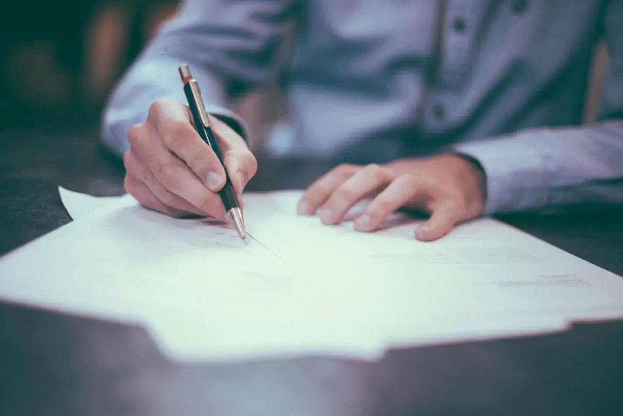 Dłoń pisze na papierze. Czy to oznacza, że firma ogłasza upadłość, co z pracownikami?