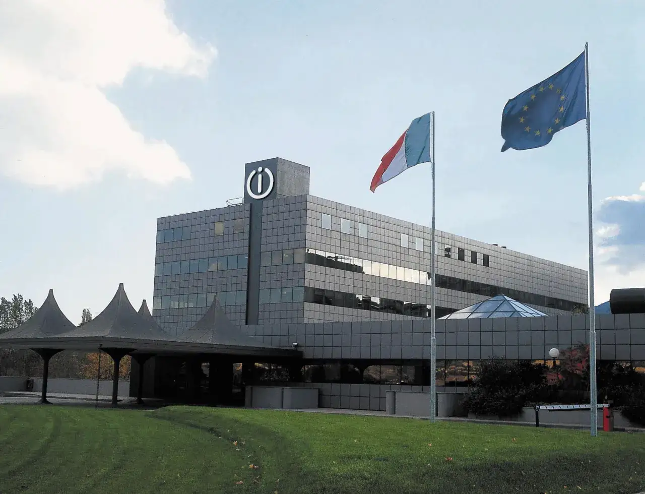 Siedziba Indesit, włoskiej firmy AGD. Flagi Włoch i UE przed nowoczesnym budynkiem.