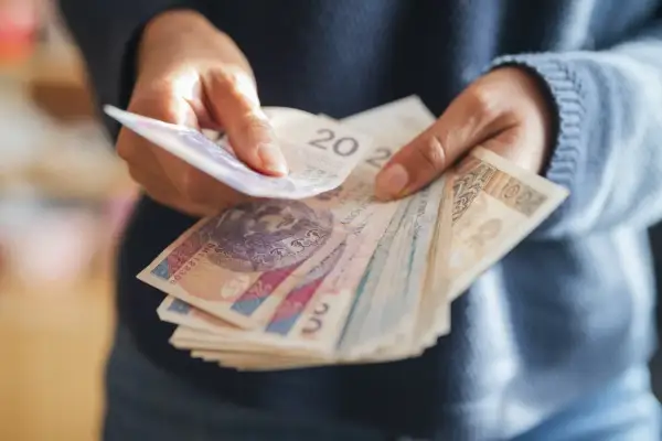 Ręce liczą polskie banknoty. Zastanawiasz się, ile wzrośnie emerytura z OFE po 65 roku życia?