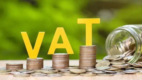 Żółte litery VAT na stosach monet, obok słoik pełen pieniędzy. Grupa vat to ważny element finansów.